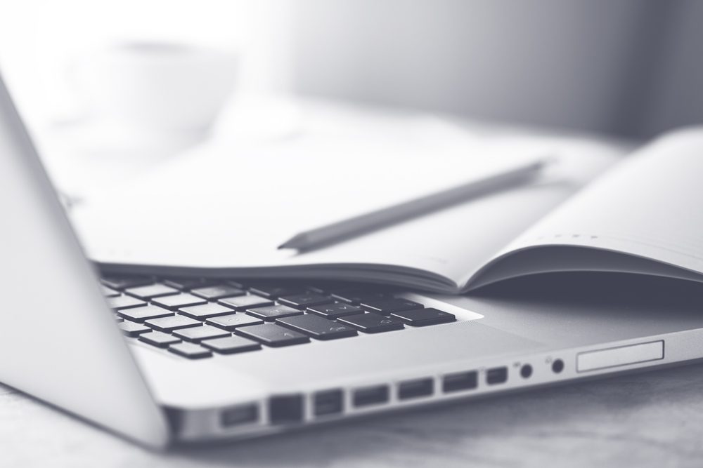 Laptop mit aufgeschlagenem Heft und Bleistift